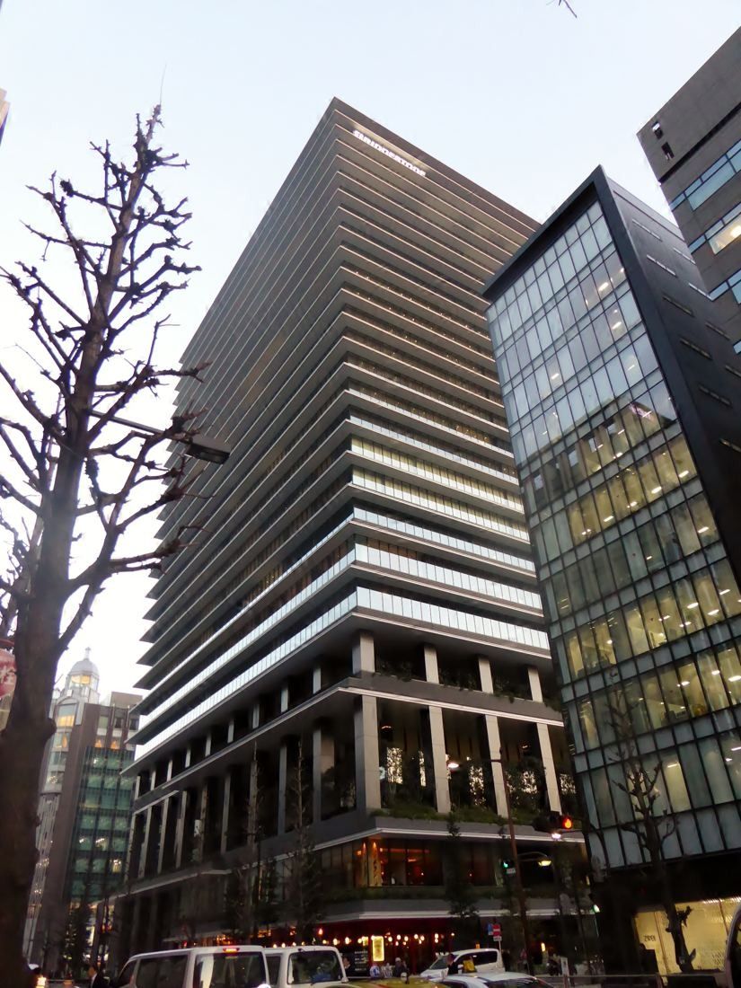 Bridgestone: The tower seen from below at a street corner, next to a neighbouring glass building