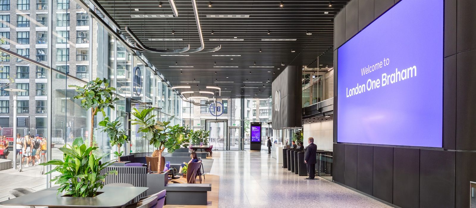 Double-height reception with plants and a large screen reading Welcome to London One Braham