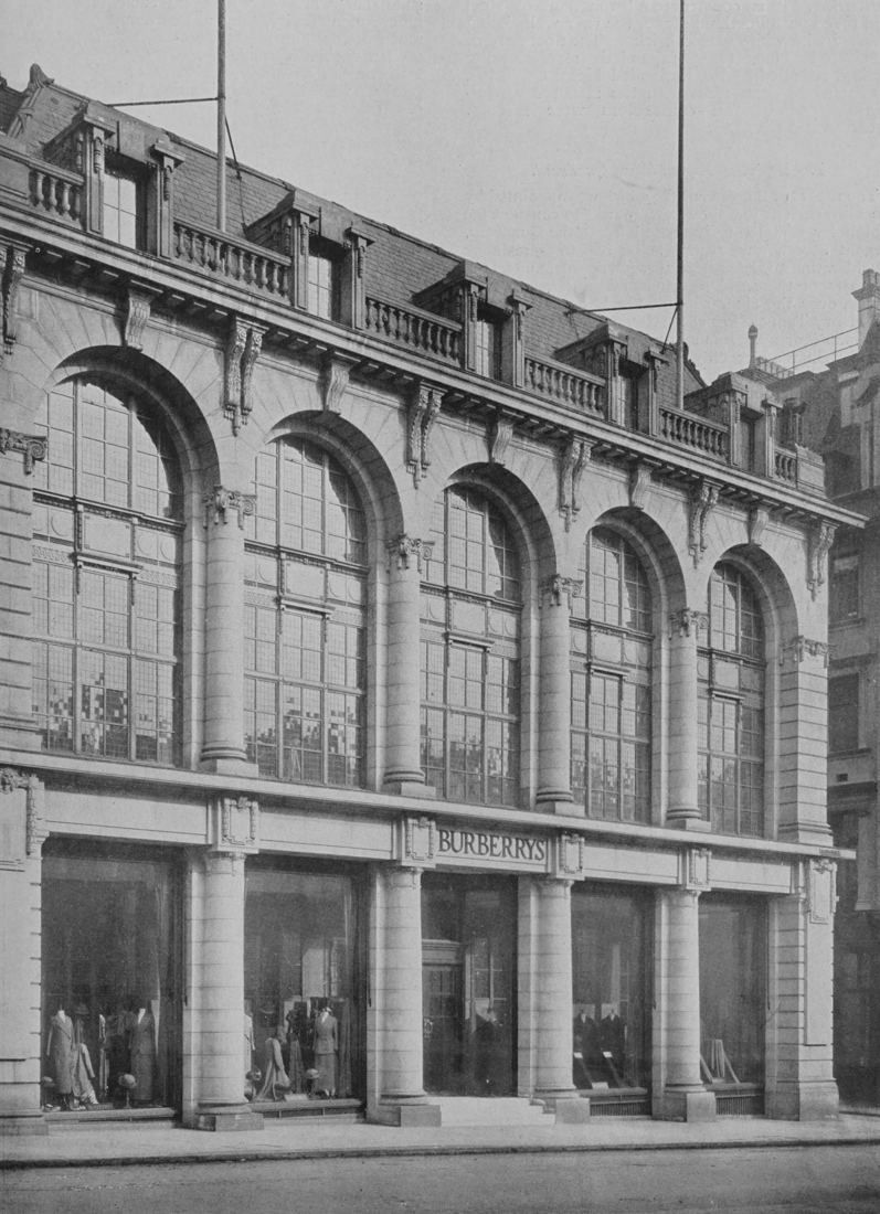 Black-and-white photo of a stone building with tall arched windows above a row of shop windows
