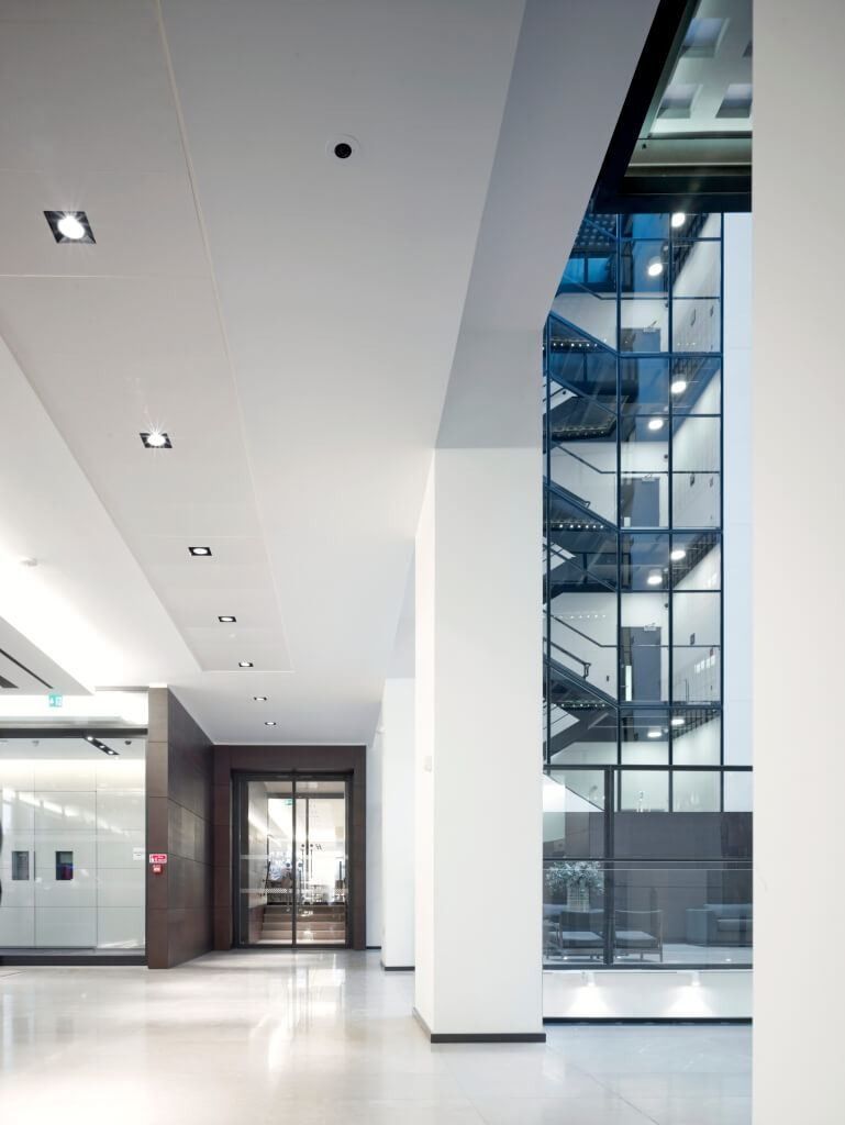 Burberry: Bright white ground-floor corridor beside a glazed stair, with a doorway at the far end