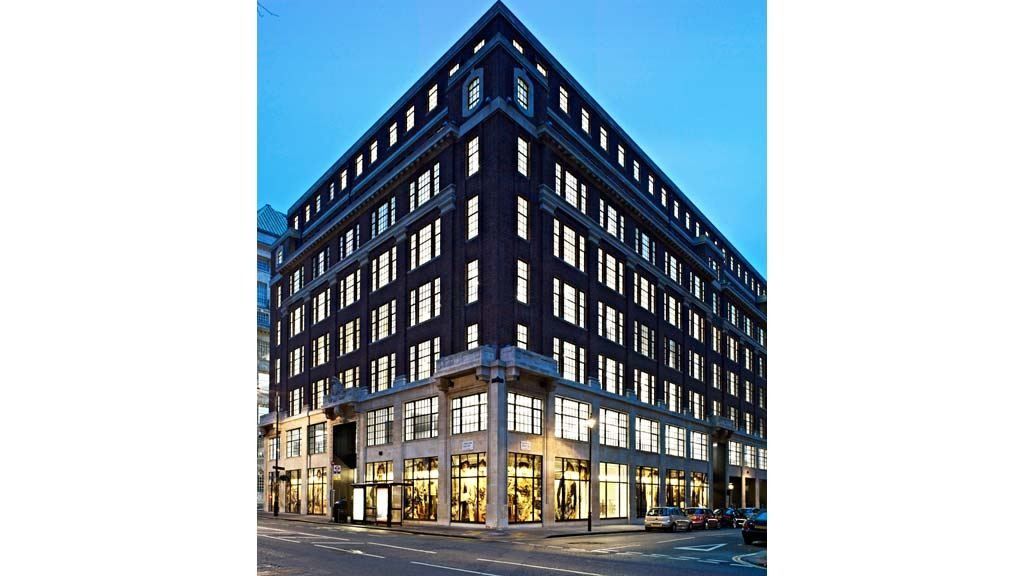 Burberry: Dark brick corner building at dusk with lit windows and glazed shopfronts at street level
