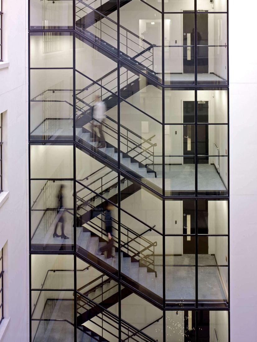 Burberry: Glazed steel staircase rising through a white atrium with gridded windows