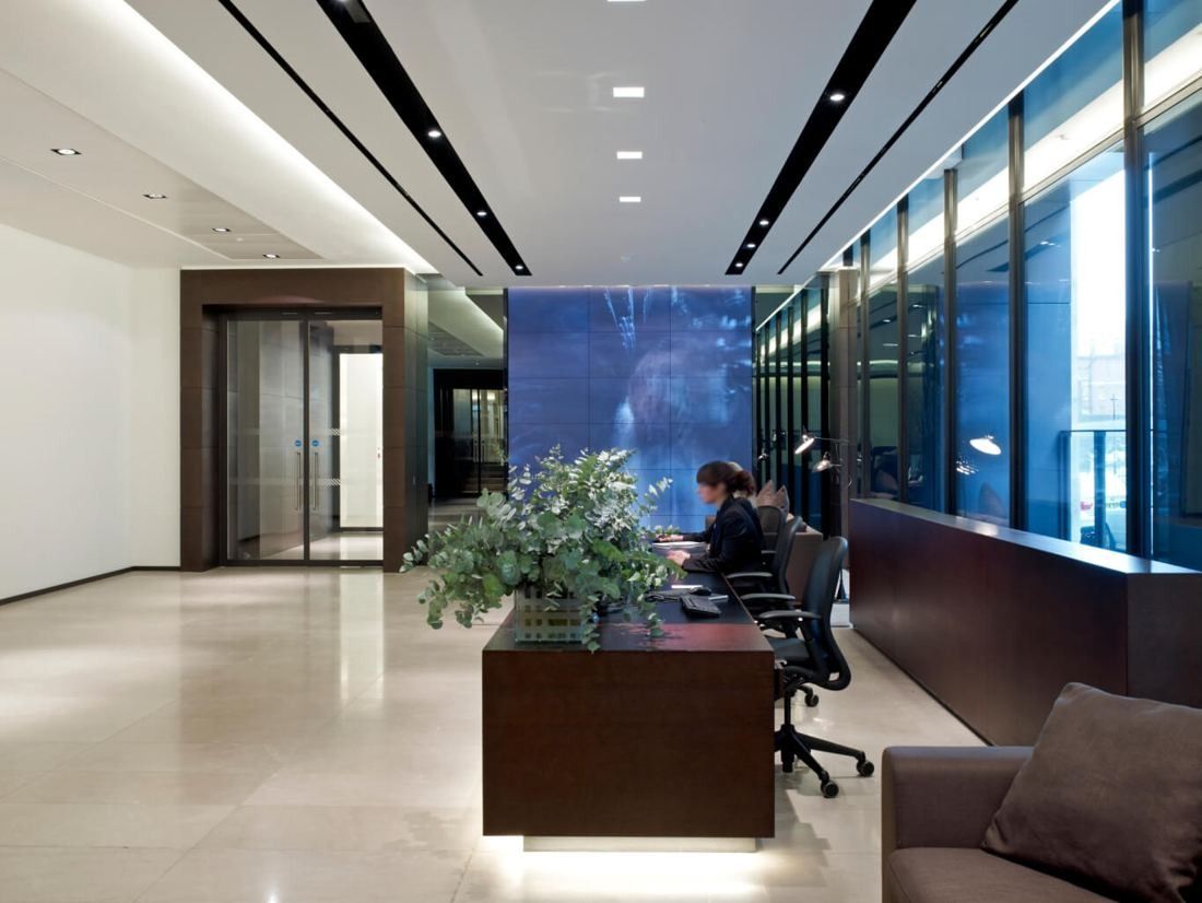 Burberry: Reception with a dark wood desk, plant arrangement, pale stone floor and a large video wall