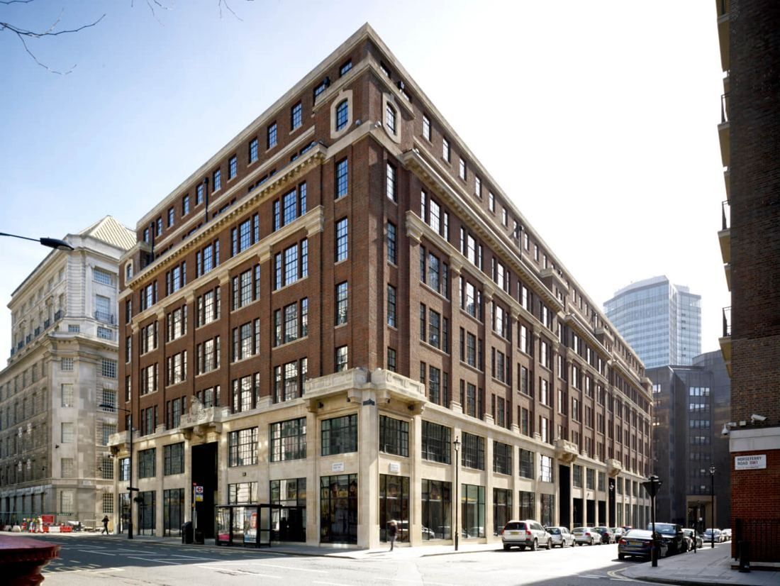 Seven-storey brick and stone corner building with large ground-floor windows on a sunny street