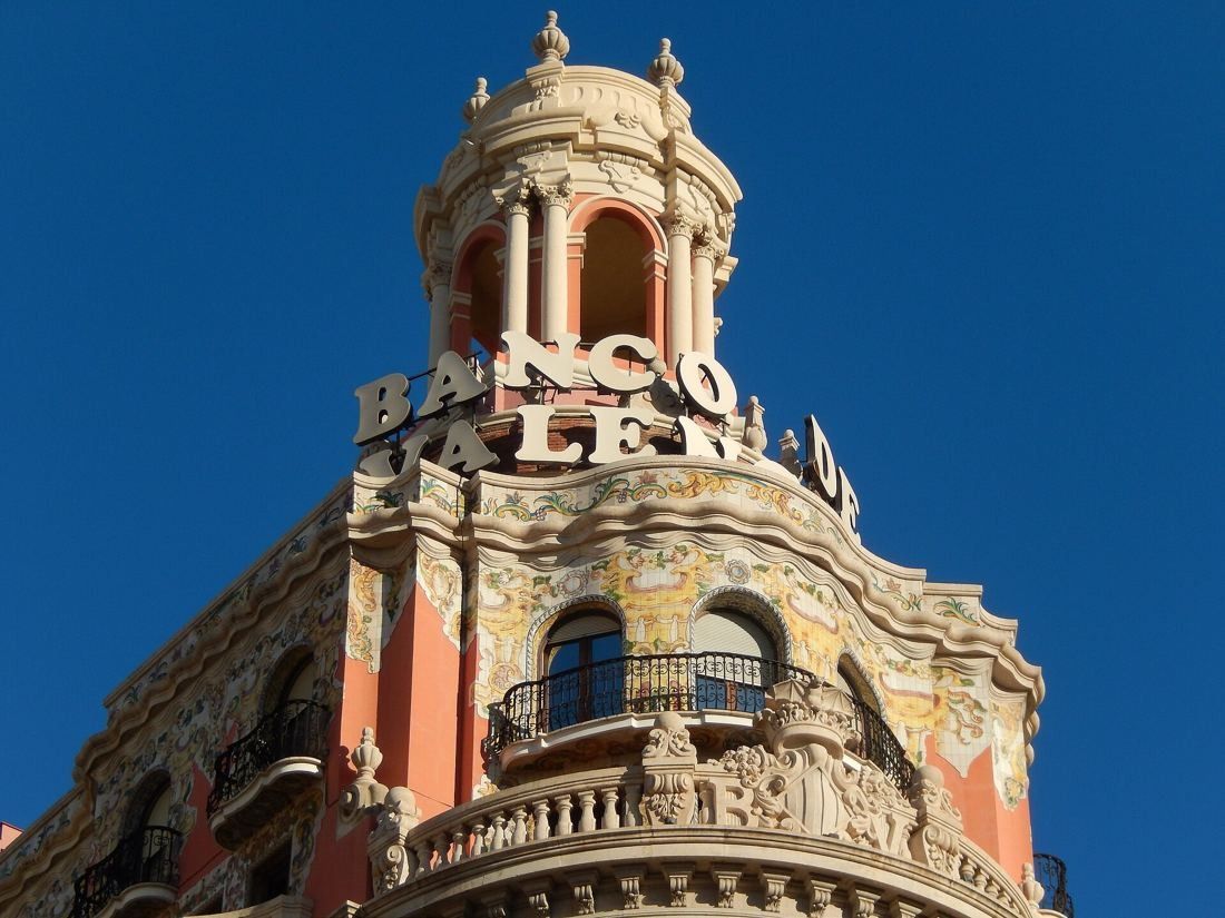 CaixaBank: Close-up of a domed corner lantern with large 'Banco de Valencia' letters against a deep blue sky