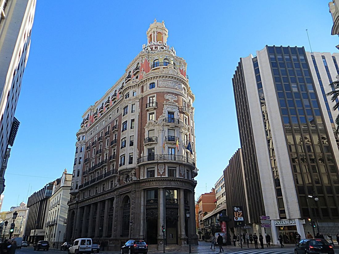 CaixaBank: Full view of the ornate corner building between modern glass office blocks