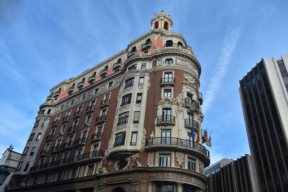 CaixaBank: Low-angle view of a long brick façade with stone balconies curving into a rounded corner under a blue sky