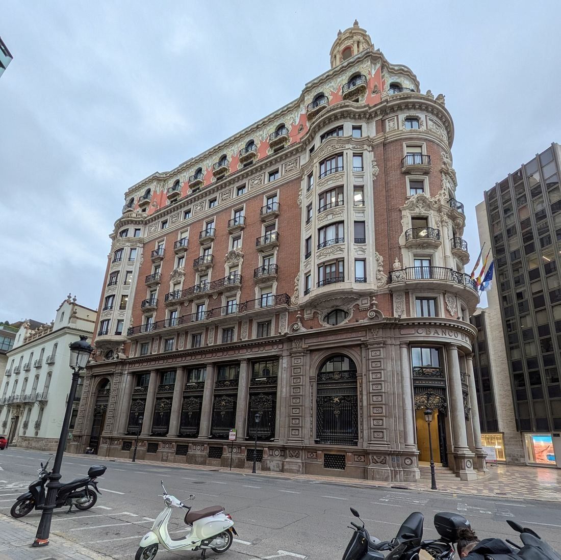 CaixaBank: Side view of the brick façade with arched ground-floor windows and scooters parked on the pavement