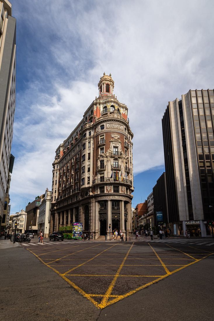 CaixaBank: The corner building at the end of a wide junction with yellow road markings