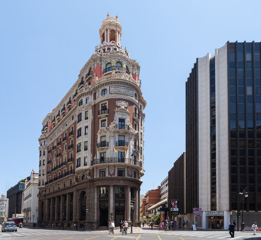 CaixaBank: The corner building in full sun beside a dark glass tower