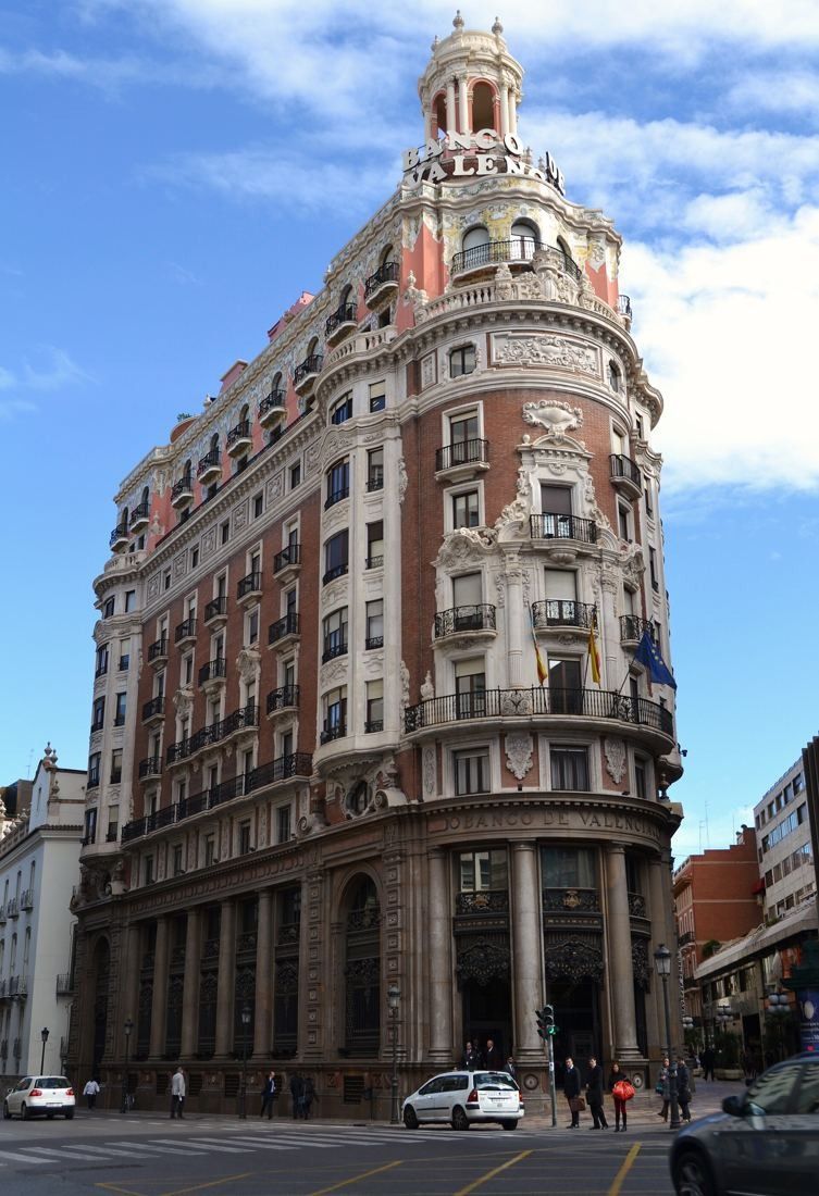 CaixaBank: The corner building with its columned ground floor under a cloudy blue sky