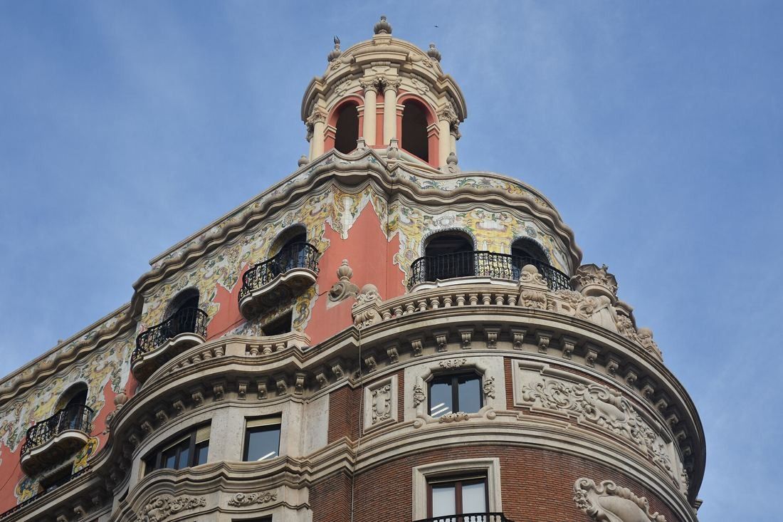 CaixaBank: Upper floors of the rounded corner with pink and cream decoration and a domed lantern