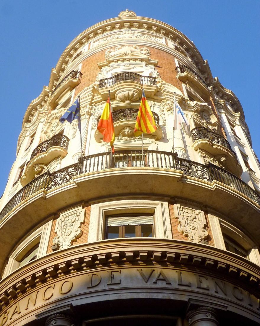 CaixaBank: Upward view of the cream-coloured round corner with balconies and flags