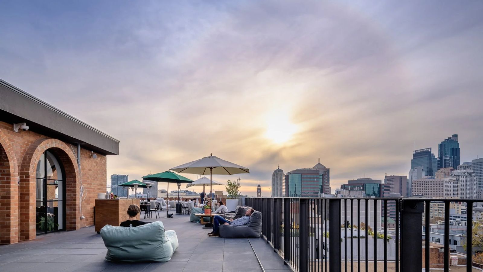 Rooftop terrace with umbrellas and bean bags facing the city skyline at sunset