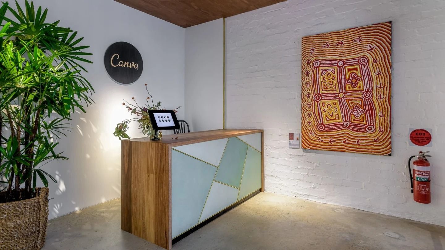 Canva: Small reception desk with a painting on a white brick wall