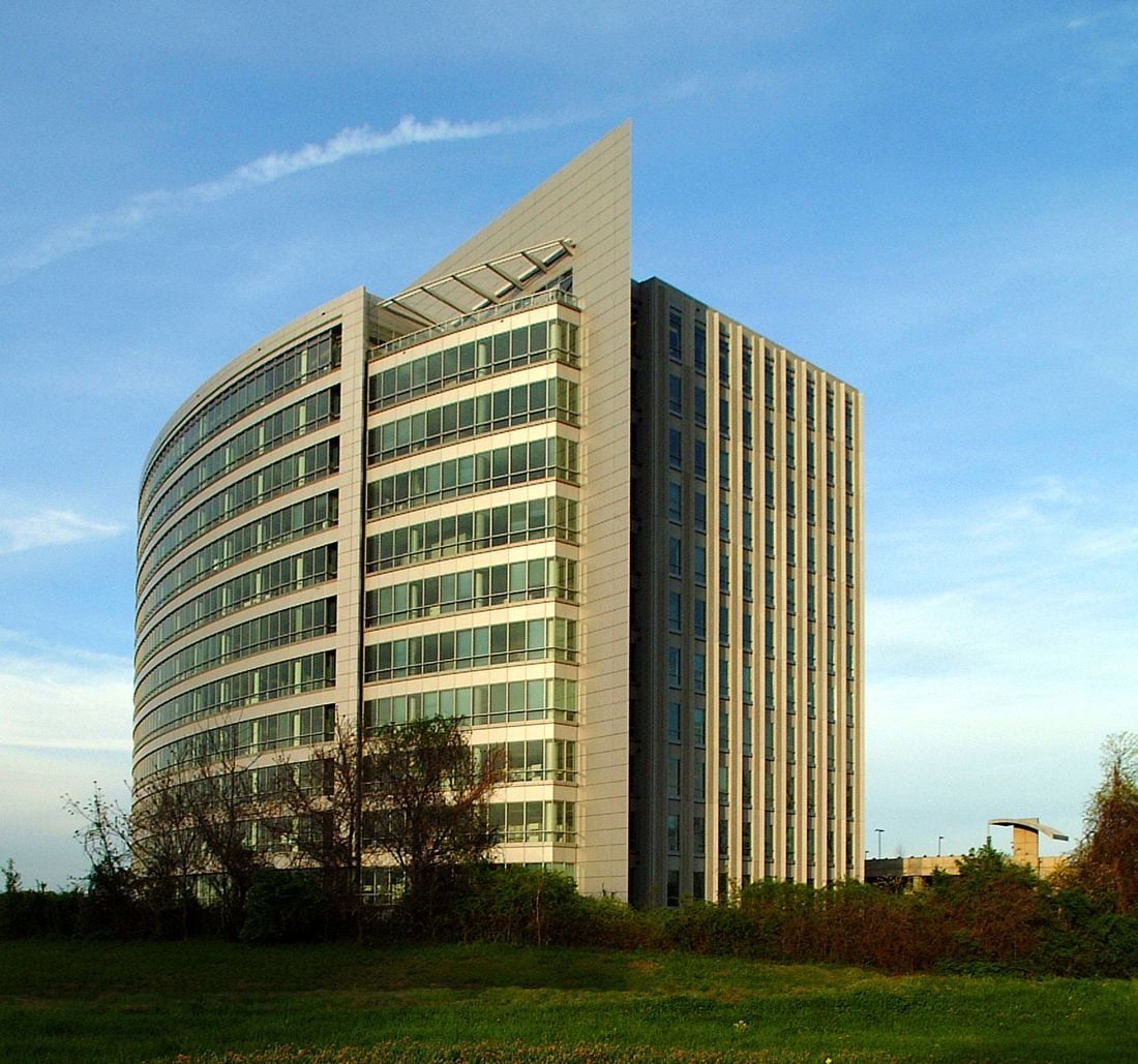 Curved glass office tower lit by low sun above a lawn