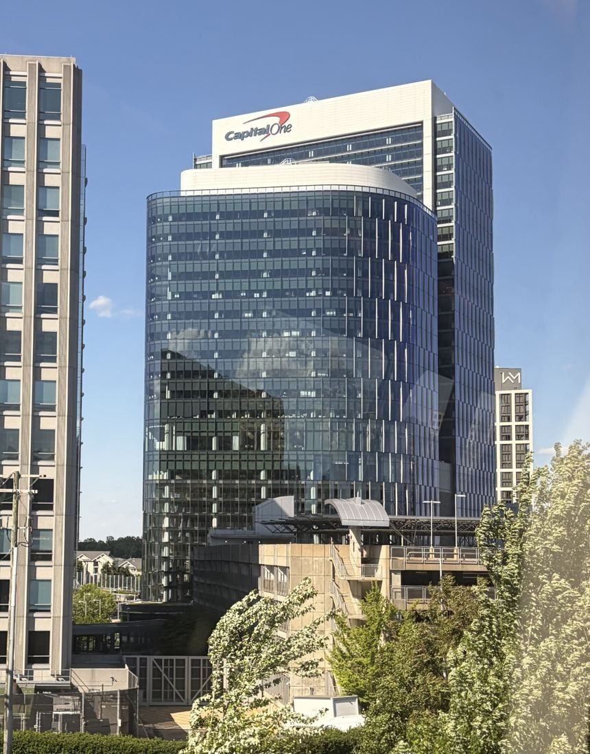Capital One: Glass office towers with a sign on the crown, seen over trees