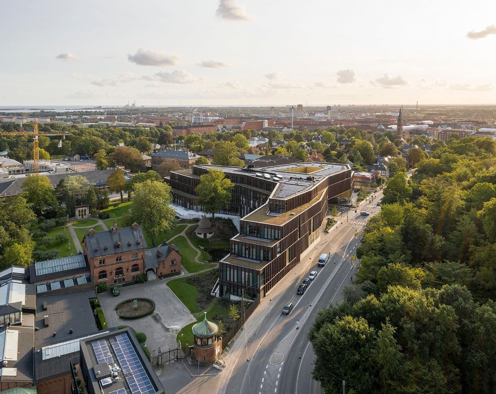 Carlsberg: Aerial view of the angled copper-coloured building among trees, older brick buildings and a road