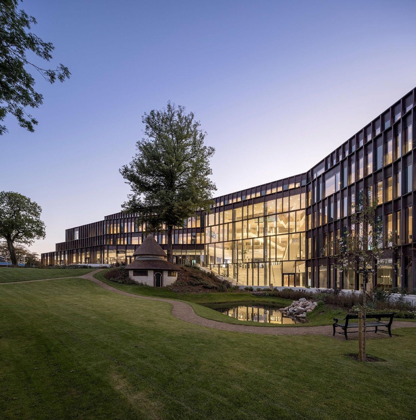 Carlsberg: Angled glazed wings at dusk overlooking a lawn and a thatched pavilion