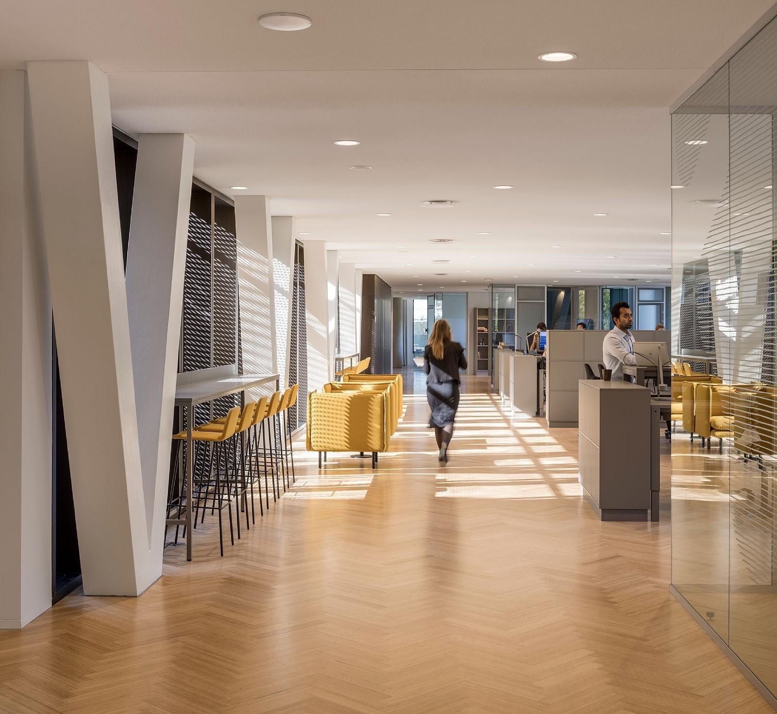 Carlsberg: Bright office floor with herringbone wood floor, angled white columns and yellow chairs