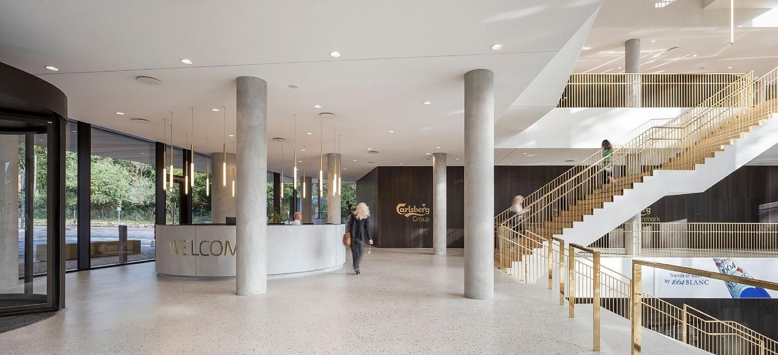 Carlsberg: Reception area with a white counter, concrete columns and a staircase with brass railings