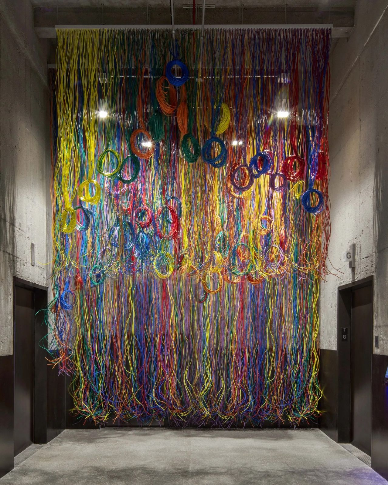 Cboe Global Markets: A tall artwork of hanging coloured cords and loops in a dark hallway