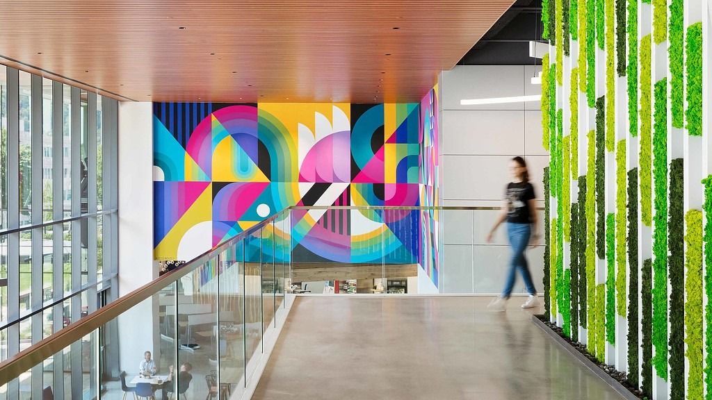 Cencora: A glass-railed walkway beside a green moss wall and a colourful geometric mural