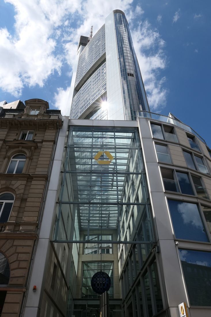 Commerzbank: Glass entrance building between older stone facades with the tower rising behind