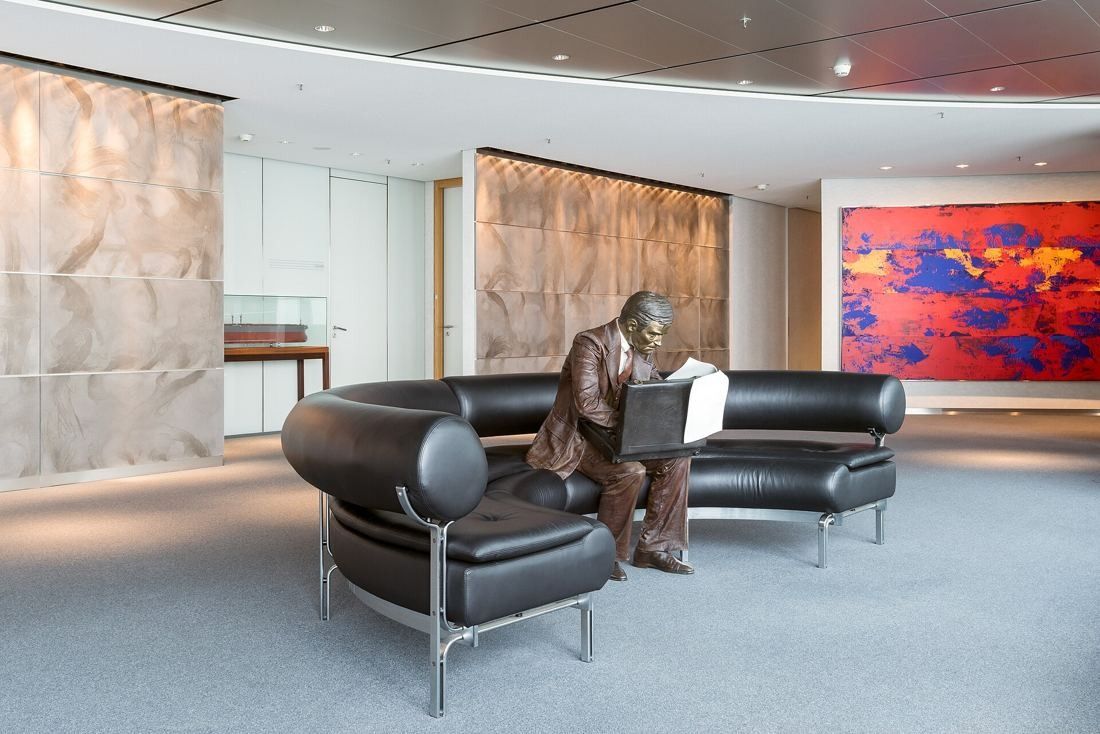 Commerzbank: Lounge with a curved black leather sofa, a bronze figure reading a newspaper and a large red and blue painting