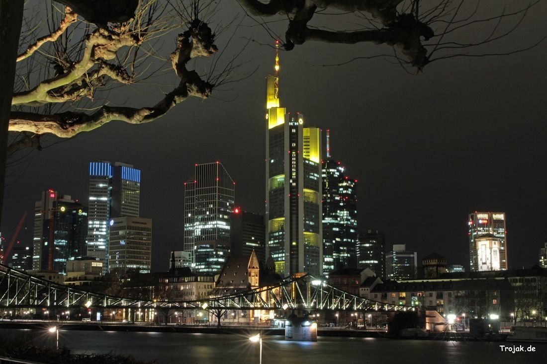 Commerzbank: Night skyline with the tower lit in yellow behind a river and a bridge