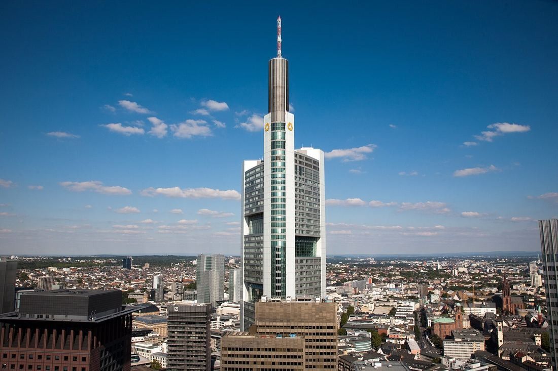 Tall slender skyscraper with an antenna mast rising above a low city under a blue sky