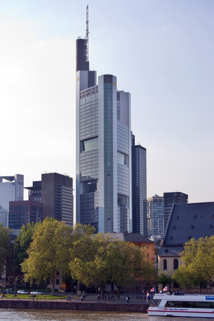 Commerzbank: Tower with stepped glass sections rising above trees along the riverbank