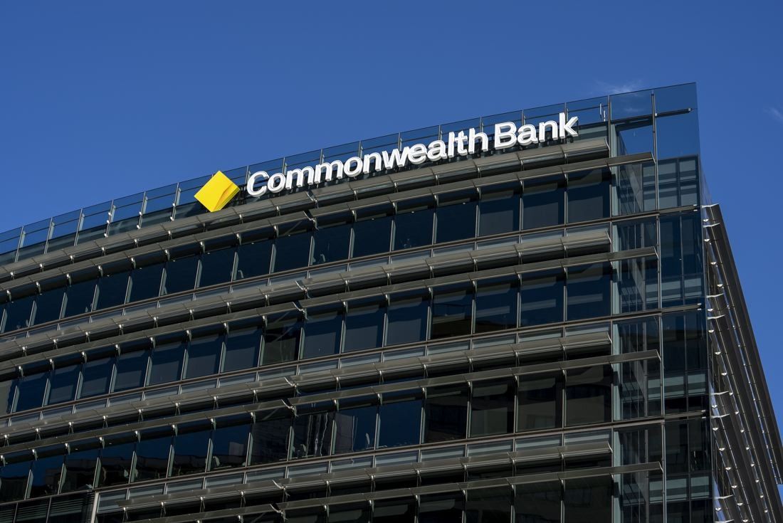 Commonwealth Bank of Australia: Corner of a glass office building with horizontal louvres under a deep blue sky, bank sign at the top