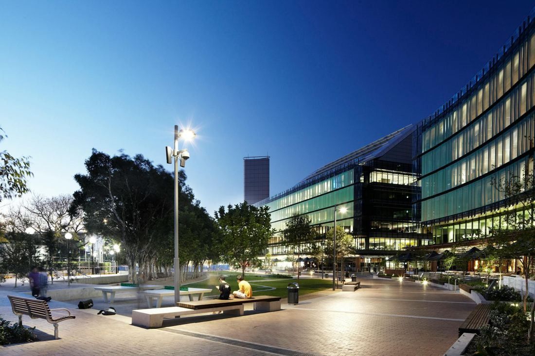 Commonwealth Bank of Australia: Paved plaza with benches and trees at dusk in front of a lit glass office building