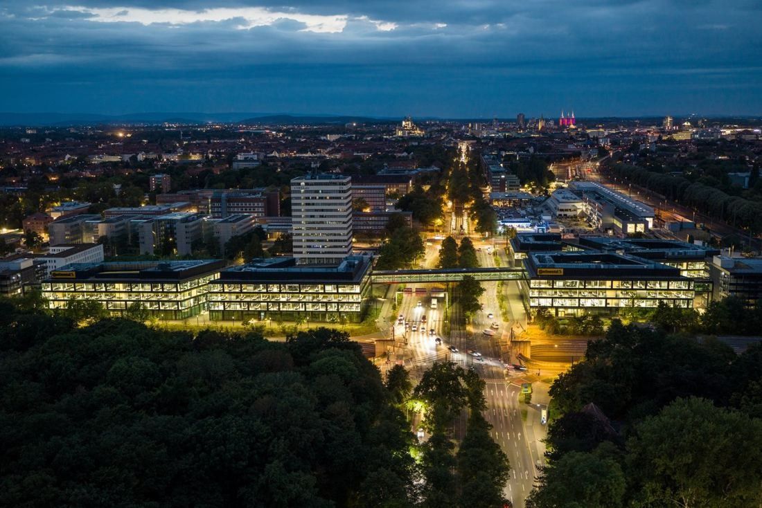 Continental: Aerial view at night of lit office buildings on both sides of a tree-lined road linked by a bridge