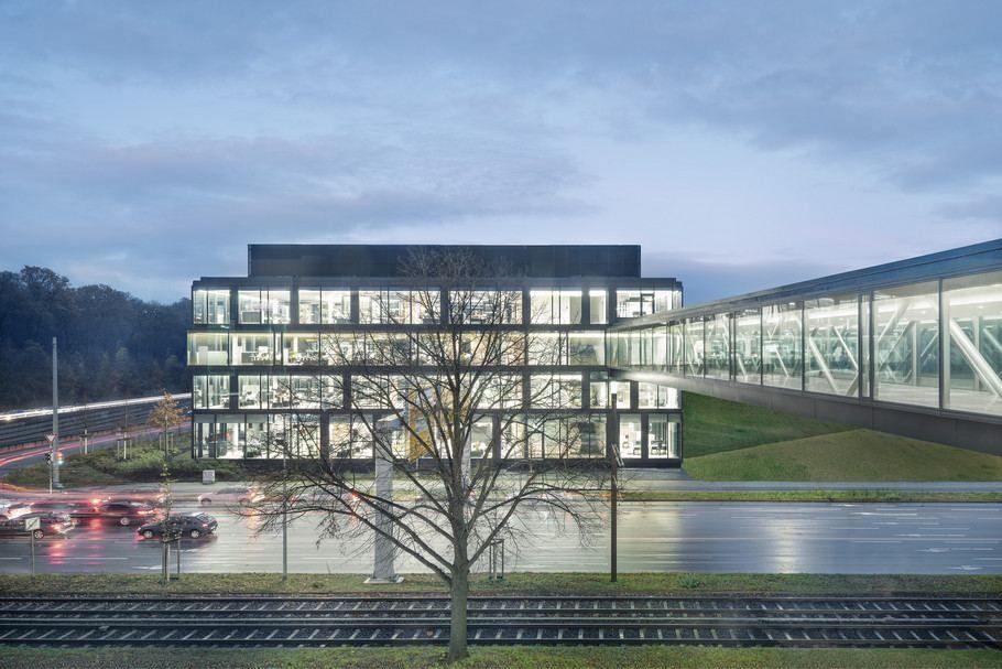 Continental: Glass office building lit at dusk with a glazed bridge leading off to the right over a road
