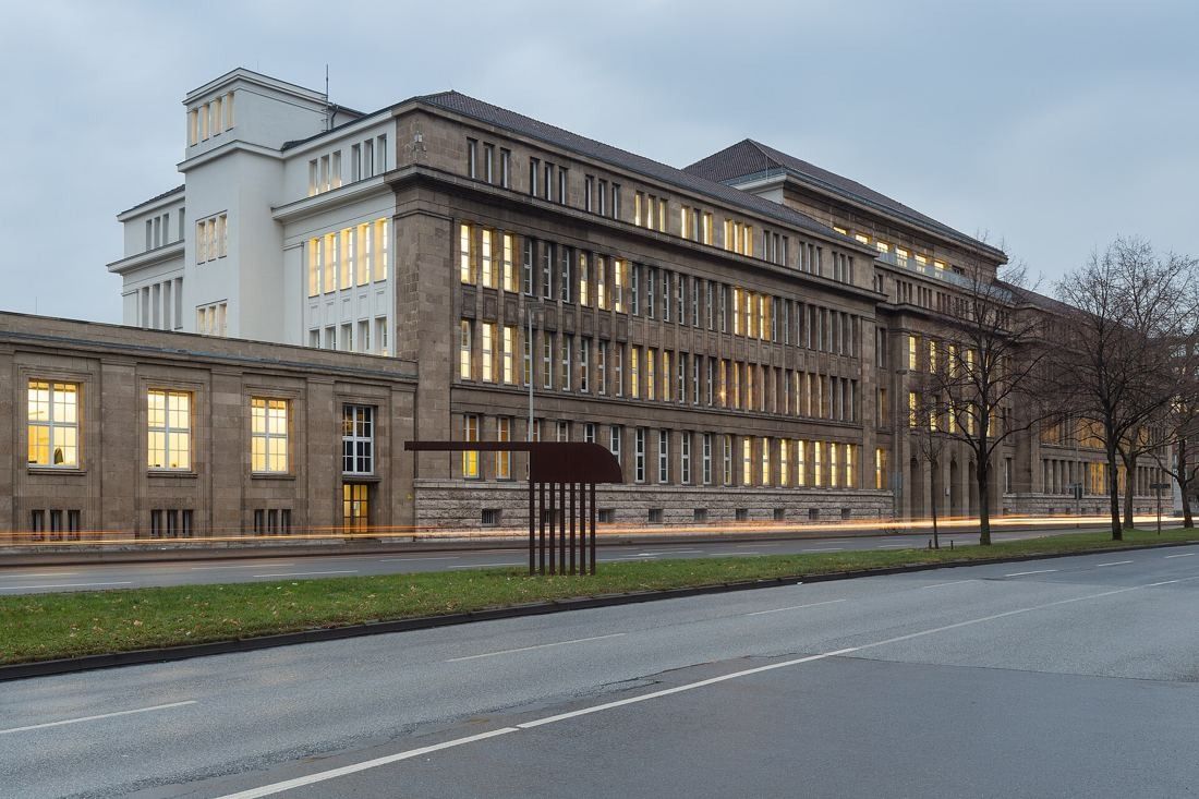 Large stone-clad administration building with rows of windows and a tower block, along a street