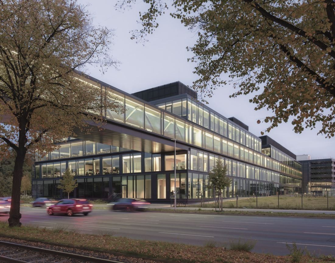 Continental: Long glass office building behind autumn trees, cars passing in front