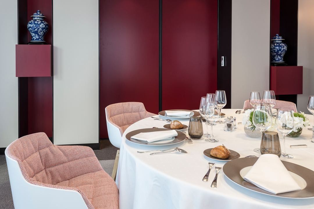 Crédit Agricole: A dining table laid with white cloth and pink chairs against dark red panels