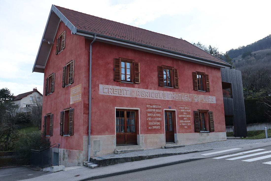 A two-storey red-rendered house with shutters and painted lettering, on a street in a valley