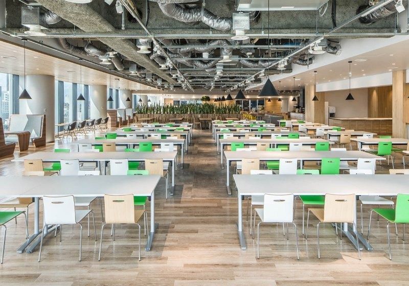 CyberAgent: Long cafeteria with white tables and green chairs under exposed ceilings