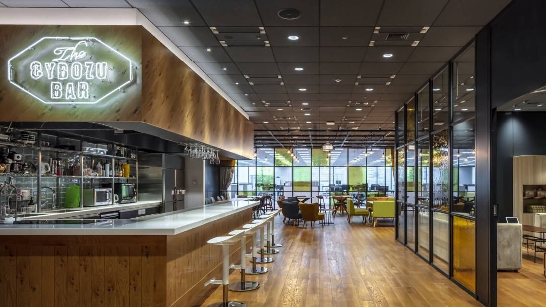 Cybozu: Bar counter with a lit CYBOZU BAR sign, wooden floor and a glass-walled room behind