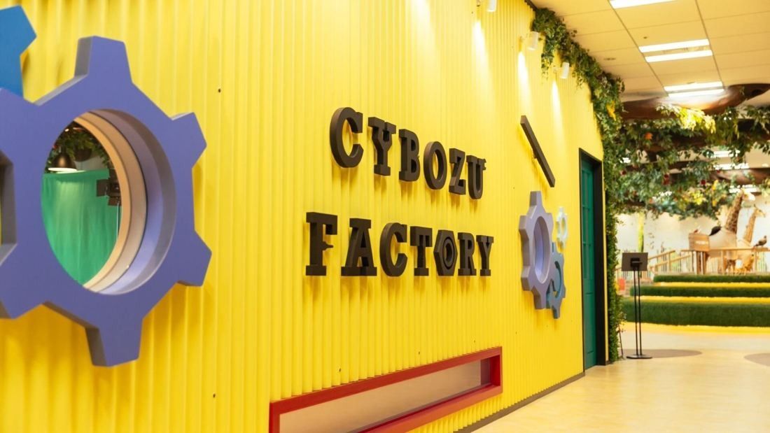 Cybozu: Bright yellow wall with a gear-shaped window and CYBOZU FACTORY lettering