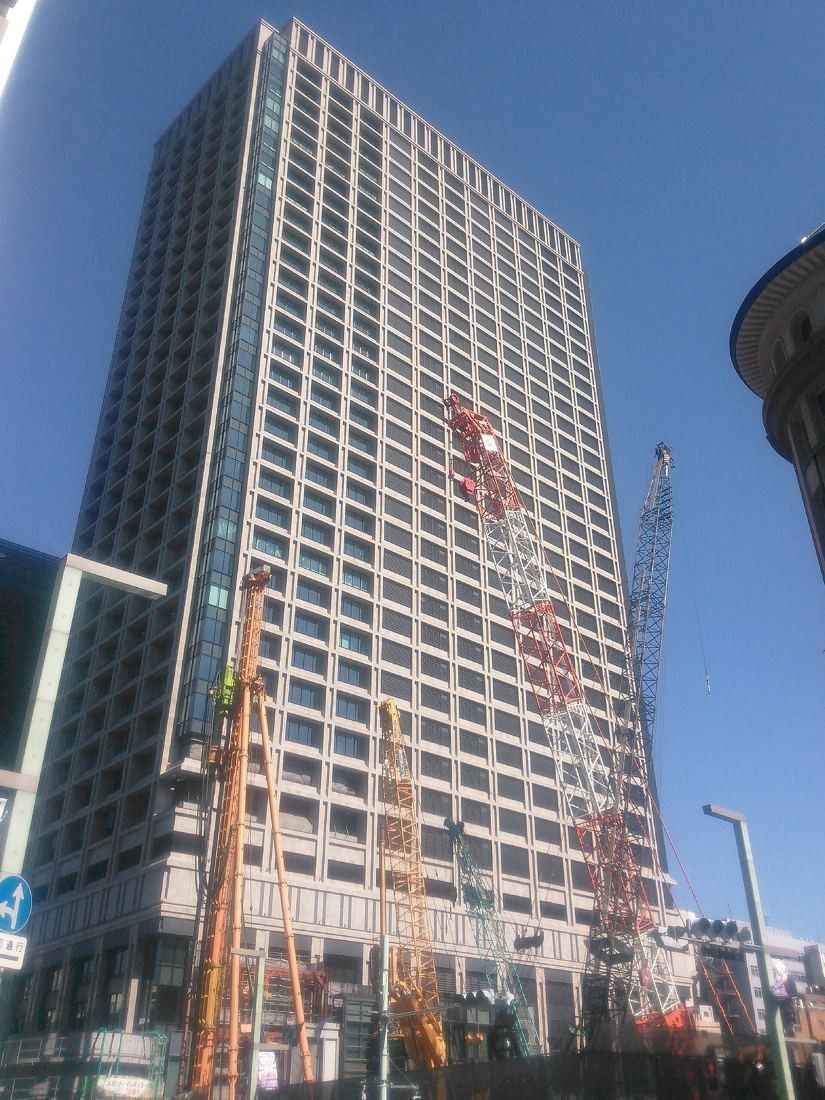 Cybozu: Glass-and-stone office tower against a blue sky, with construction cranes beside it