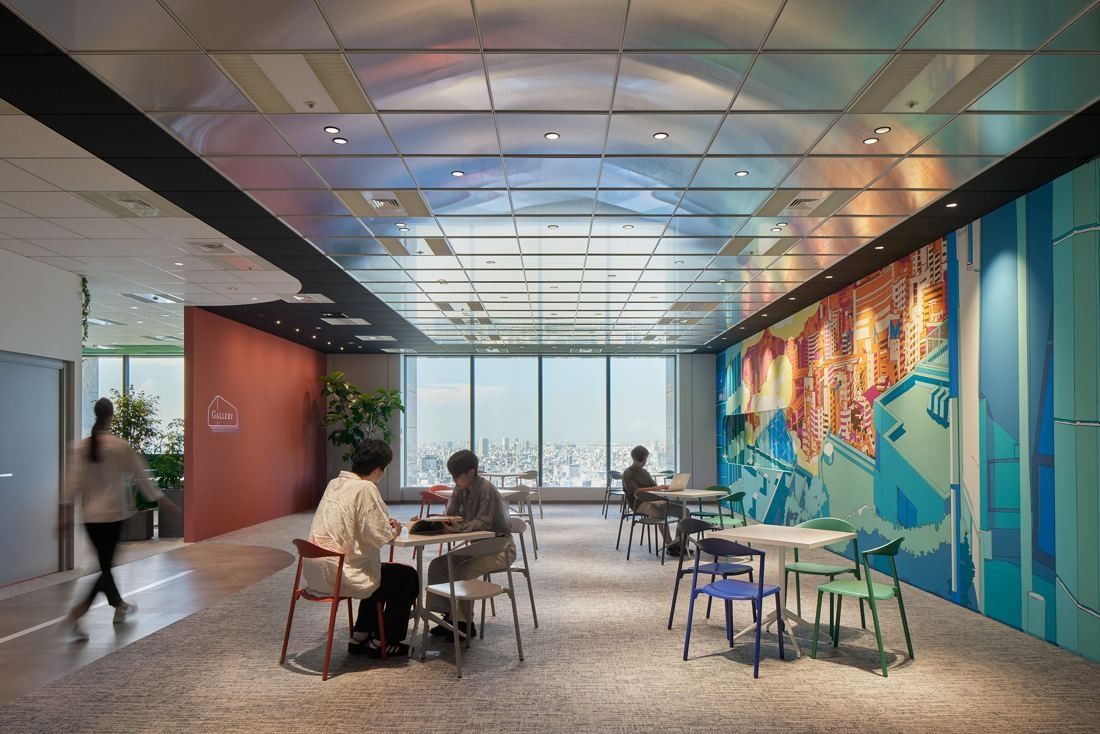 Cybozu: Long room with tables and chairs beside a wall-length illustrated mural and windows