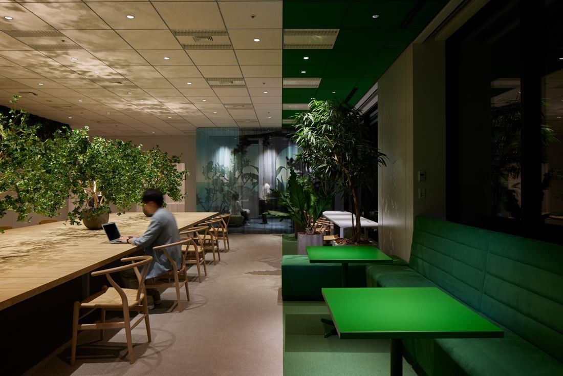 Cybozu: Long wooden counter desks with plants and green upholstered booths