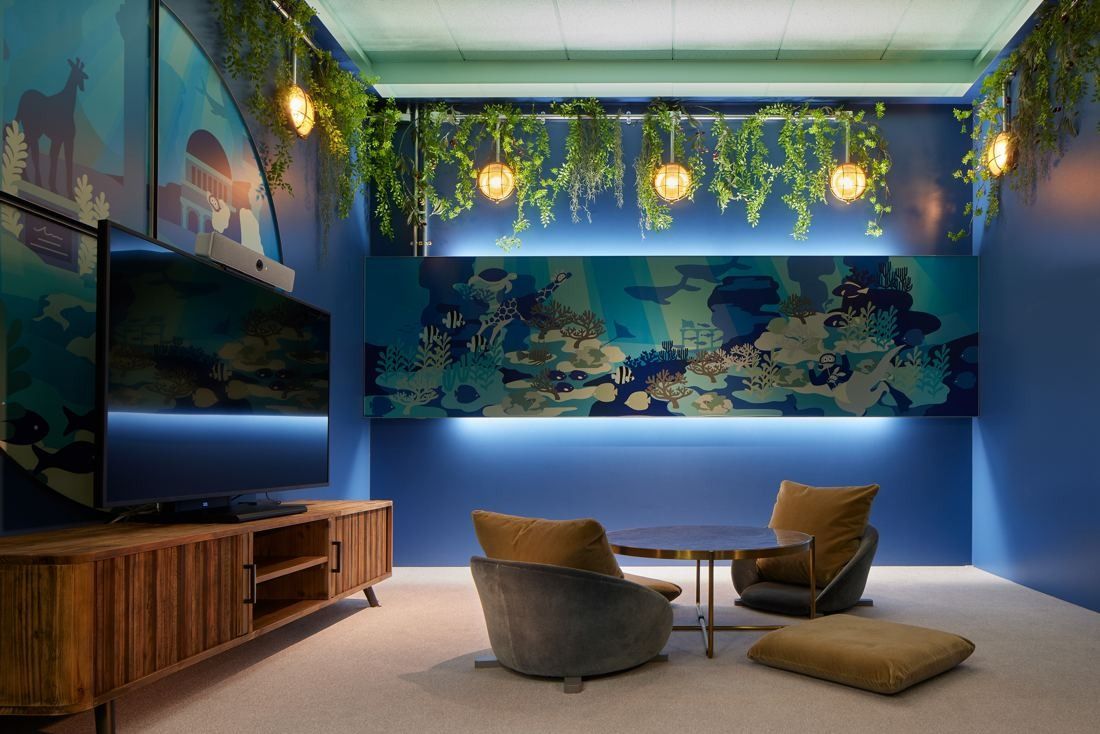 Cybozu: Lounge with armchairs, floor cushions and a TV in front of a dark blue wall with an underwater mural