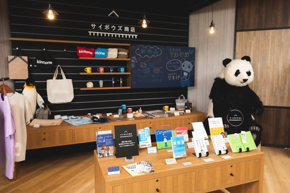 Cybozu: Shop corner with branded bags, books and goods on wooden shelves and a panda figure