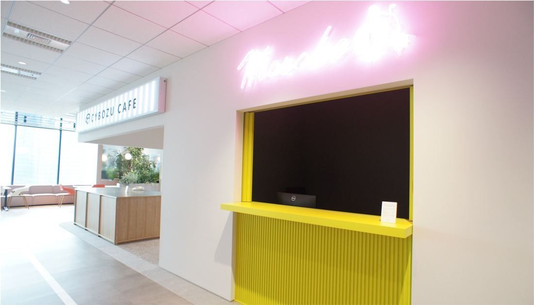 Cybozu: White café counter with a pink neon sign and a yellow service window