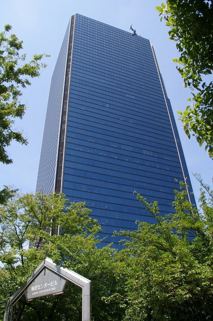 Dark blue glass high-rise seen from below between green trees